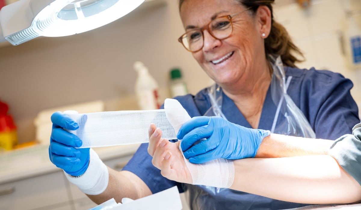En kvinna i operationskläder lindar bandage om en hand.