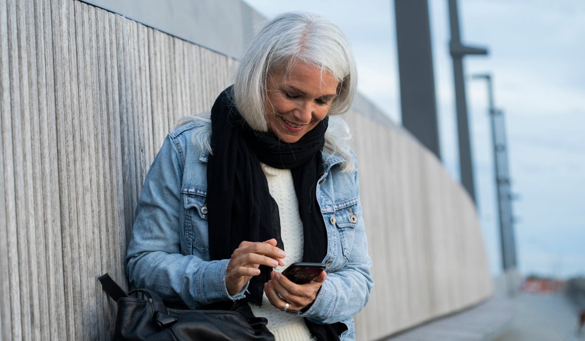 En kvinna sitter på en vägg och tittar på sin mobiltelefon.