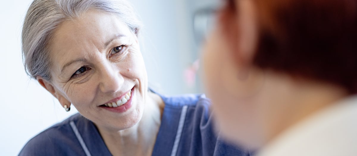 En äldre kvinna ler medan hon pratar med en yngre kvinna.