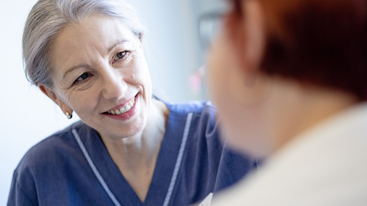 En sjuksköterska ler medan hon pratar med en patient.