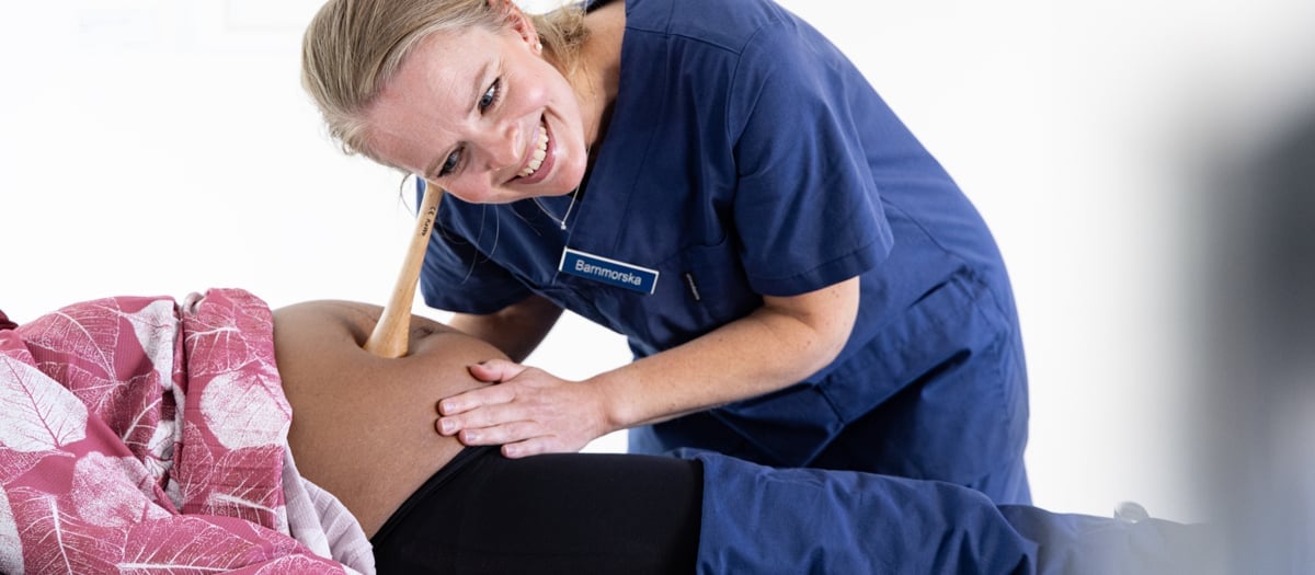 En gravid kvinna ligger på en brist och blir undersökt på magen av en barnmorska.